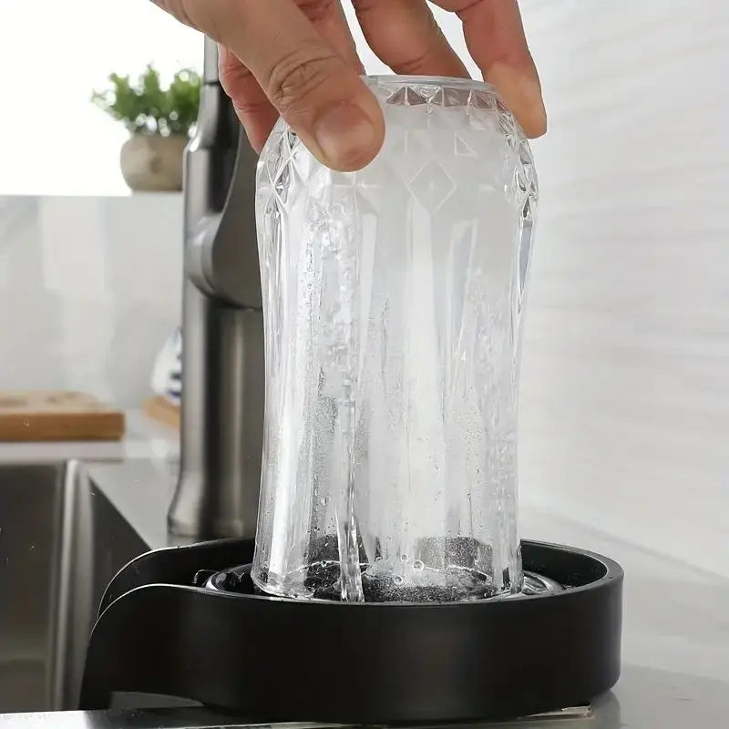 Hand pressing a glass down onto the High-Pressure Cup Washer at a kitchen sink, jets rinsing the inside